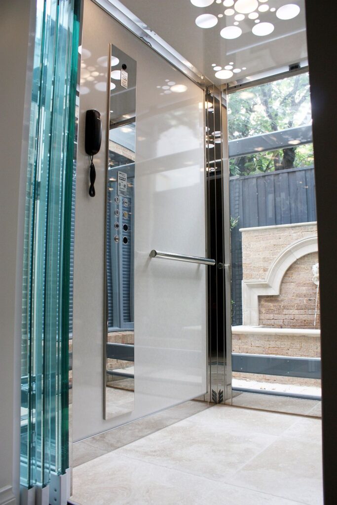 Inside the glass E2 lift cabin in the Toorak courtyard, with a stone floor and a ceiling of small lights