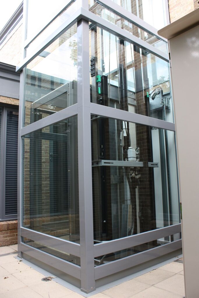Glass home lift shaft with a grey powder-coated frame standing in a courtyard in Toorak