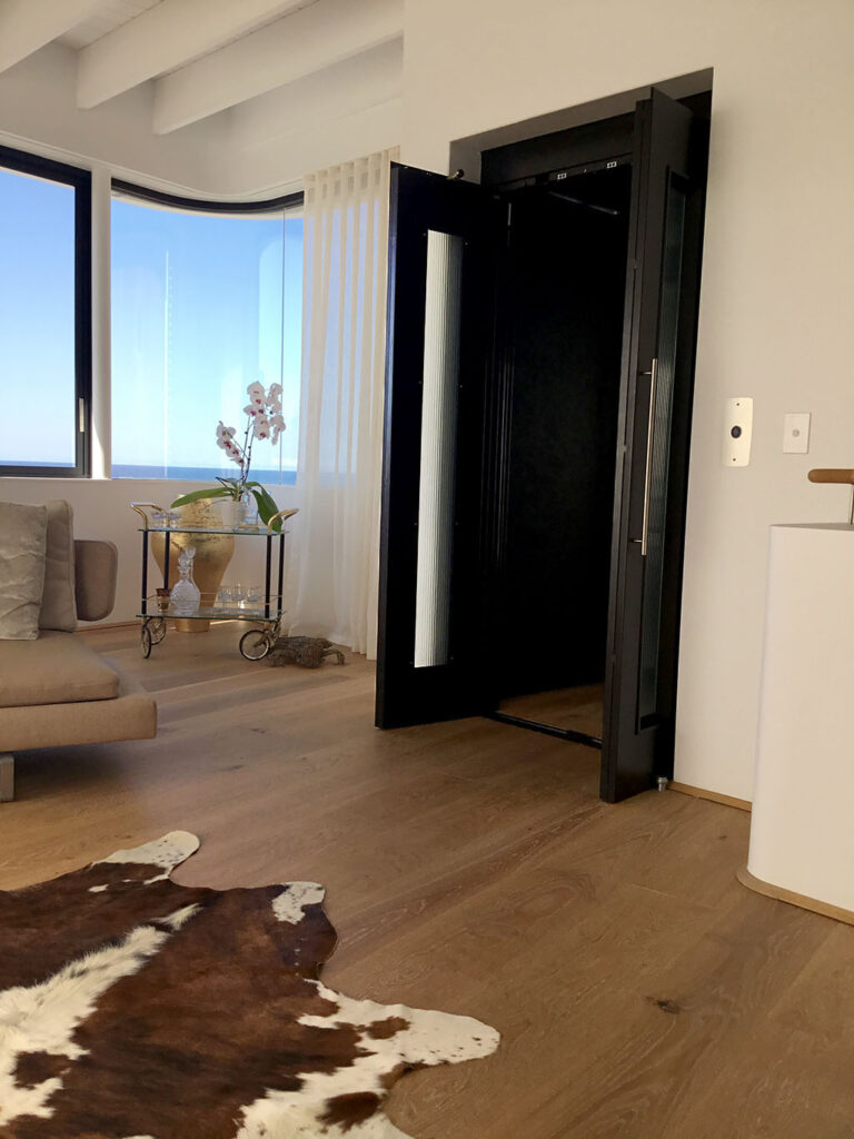 Open black lift door beside a cowhide rug and a curved window in Tamarama