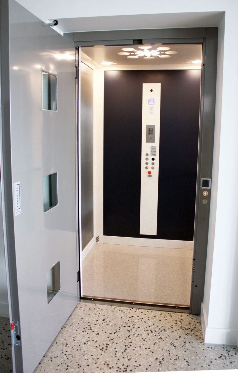 Open lift with a black rear panel, steel button strip, speckled stone floor and a star-pattern ceiling light