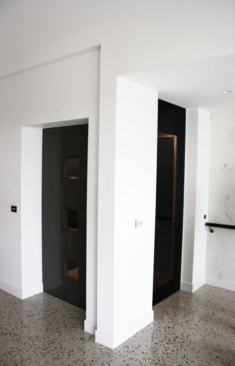 White hallway with two dark lift doors set in recesses and a polished concrete floor