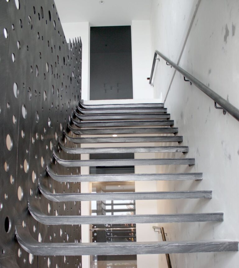 Looking up the cantilevered steel stair treads beside a black perforated steel wall
