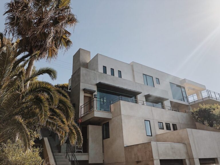 Multi-storey post-modern concrete and render home among palm trees, with stacked geometric forms and glass balconies