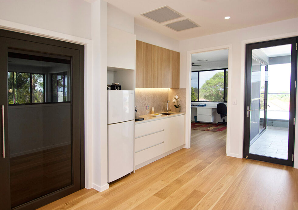 Kitchenette and hallway with the dark lift door on the left and a glass door out to the balcony