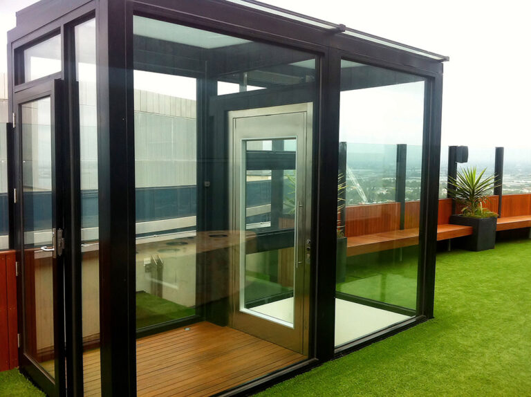 Glass lift enclosure with a glass door and timber floor on a rooftop terrace in Melbourne