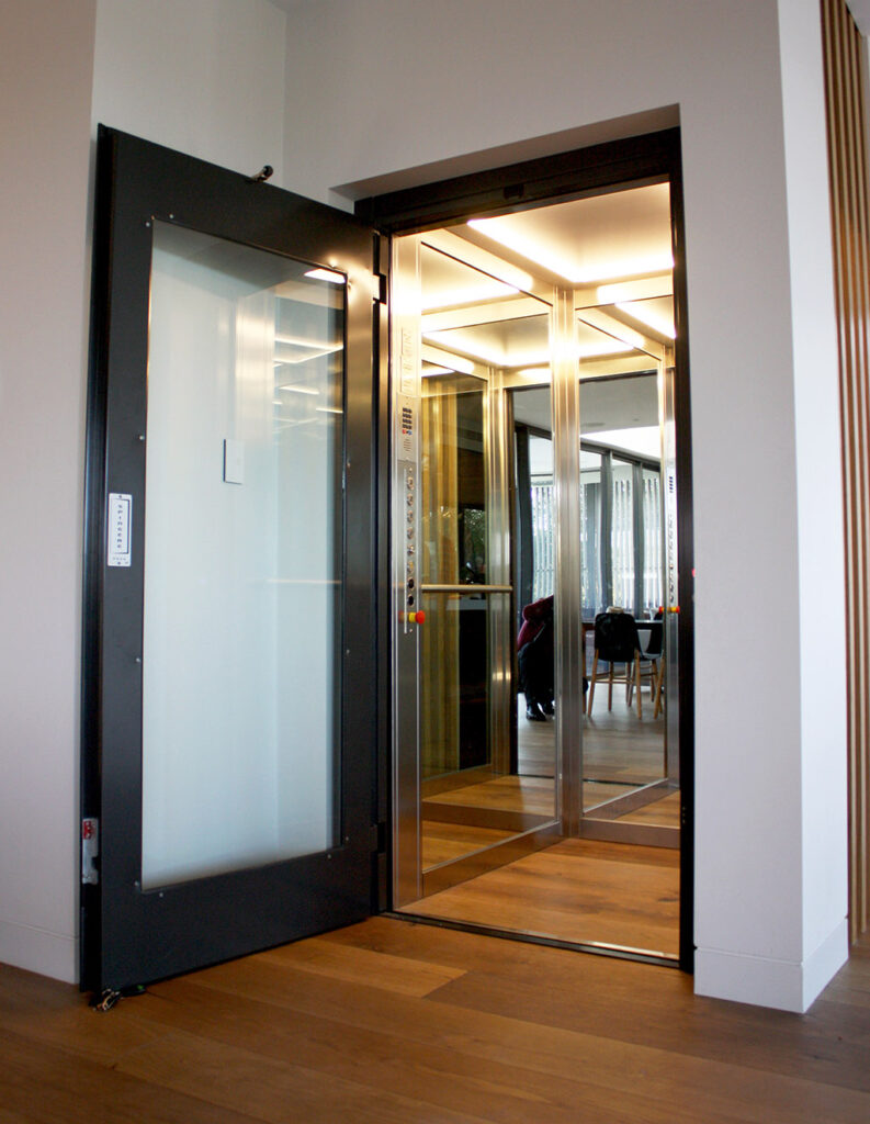Lift door with a black frame and frosted glass panel opening onto a timber floor