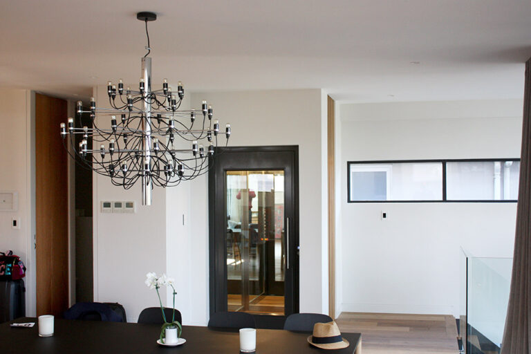 Dining area with a chandelier and the black-framed home lift door in the background