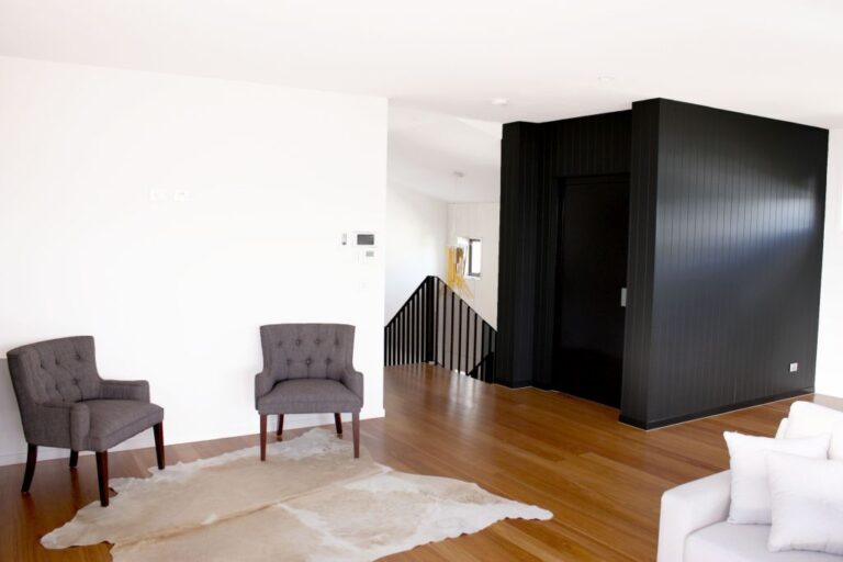 Living area in the charcoal Coorparoo home with two grey armchairs, a cowhide rug and the black clad lift shaft
