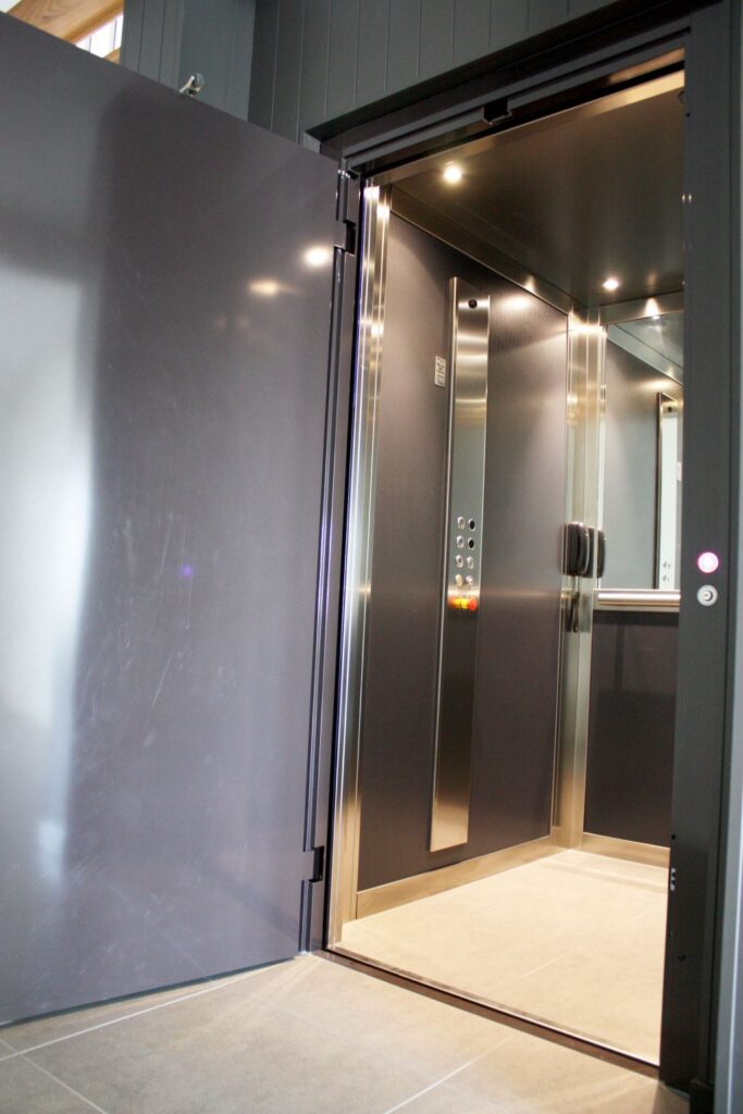 Elfo E1 landing door swung open to a charcoal cabin with downlights and a stainless steel control panel