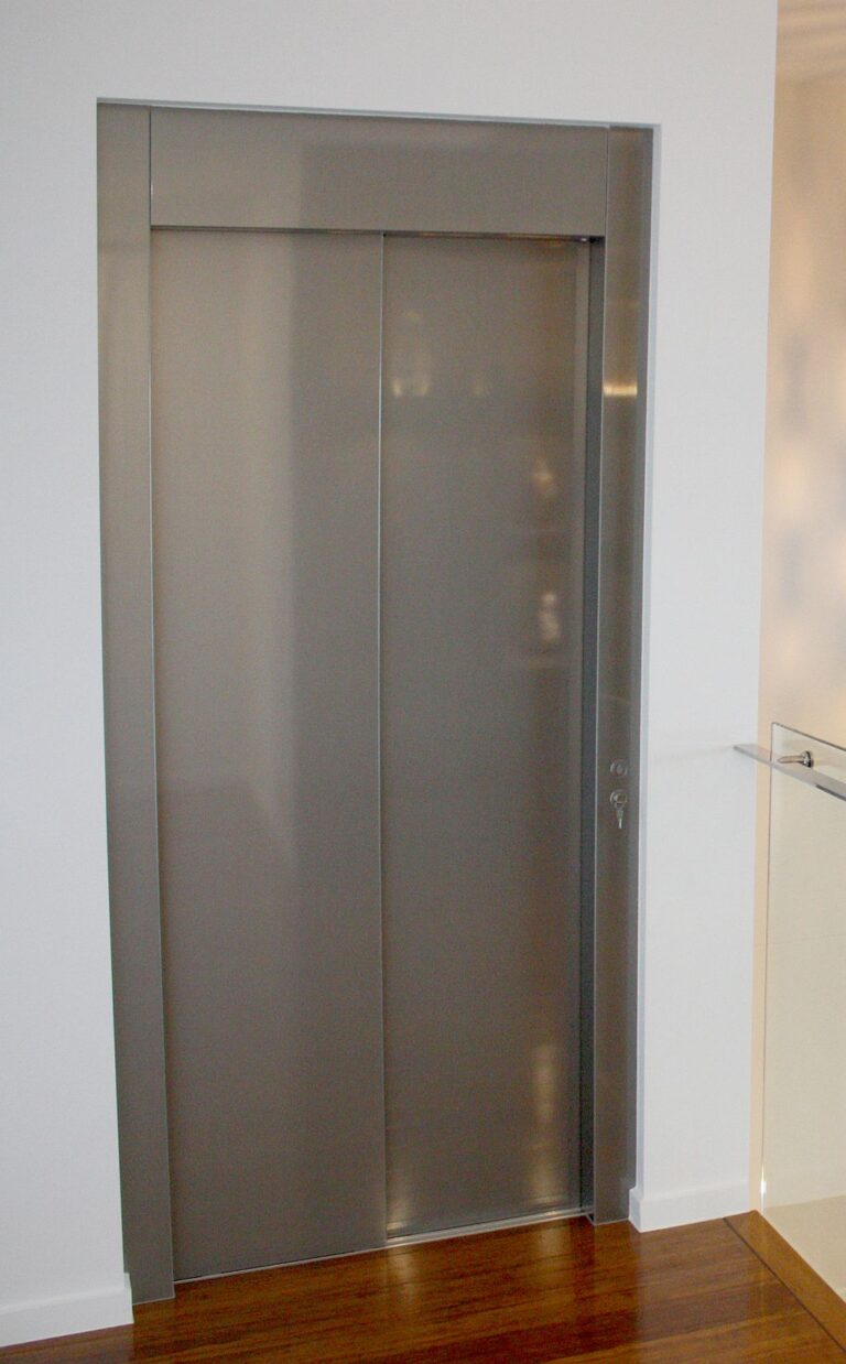 Closed stainless steel lift door with a dark frame above a polished timber floor