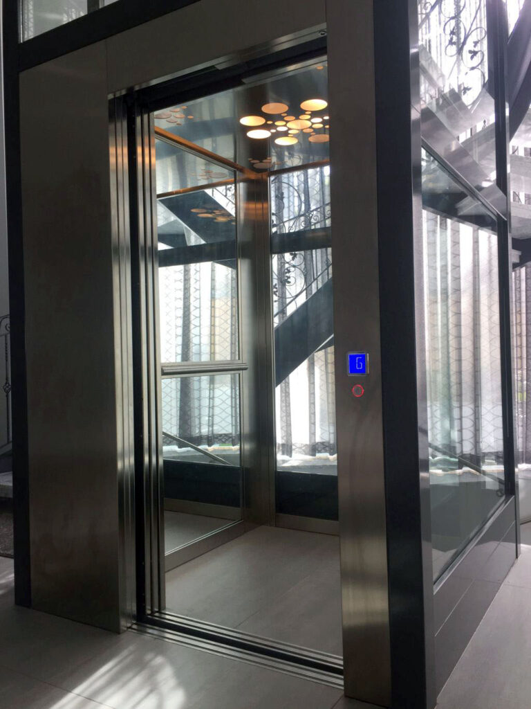 Bronze-clad lift door with a glass panel looking through to the curved staircase beyond