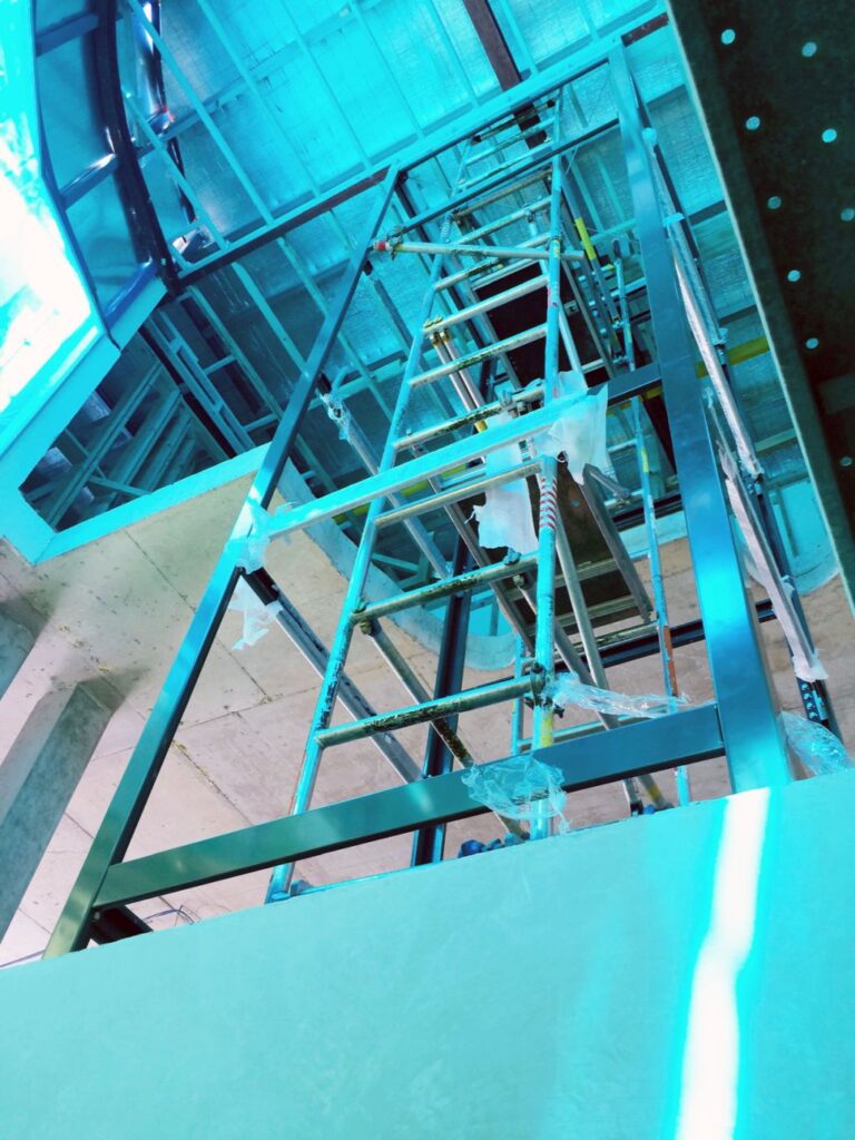 Steel lift frame seen from below with scaffolding inside the shaft during installation