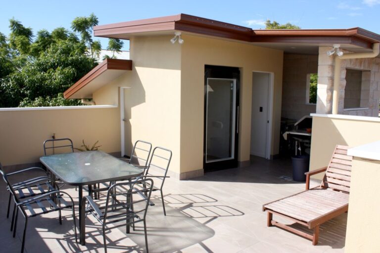 Rooftop terrace with an outdoor dining setting and lounger beside a glass door in Coorparoo