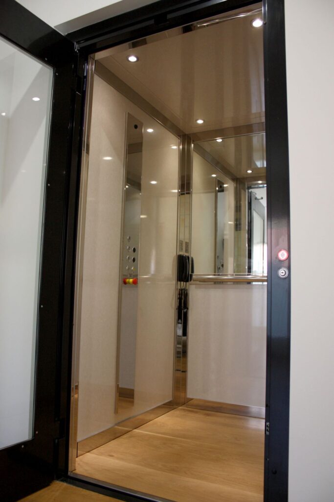 Inside the E1 home lift with creamy skinplate walls, a half-height mirror and a timber floor, seen through the black framed door