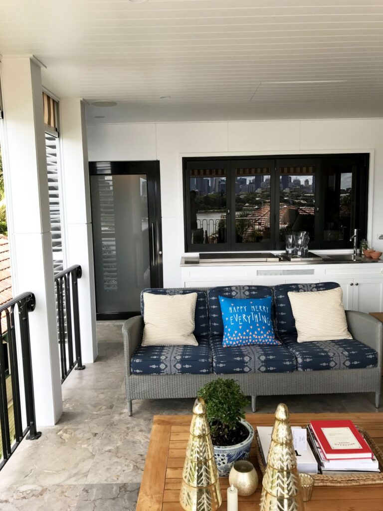 Black framed frosted glass lift door set into a white wall on the balcony, beside the sofa and a bi-fold window