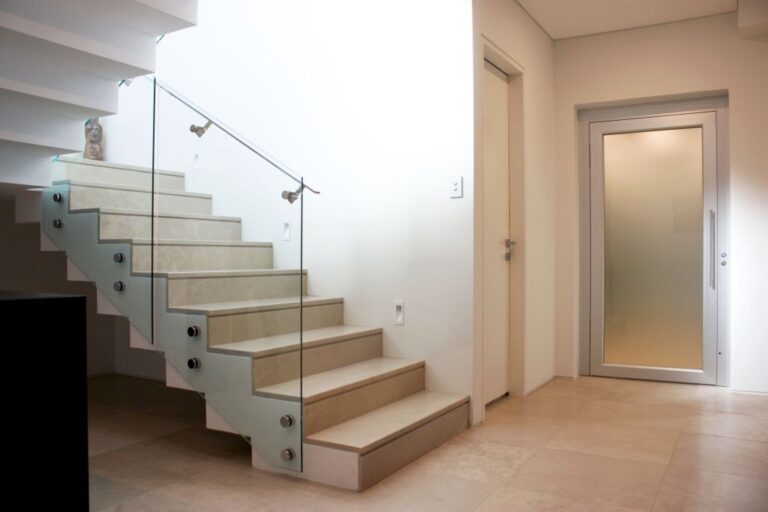 Stone tiled staircase with a glass balustrade beside a frosted glass lift door