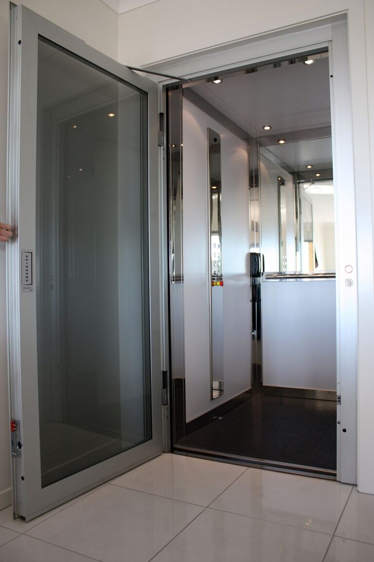 Open glass-panelled lift door with a grey frame on a white tiled floor