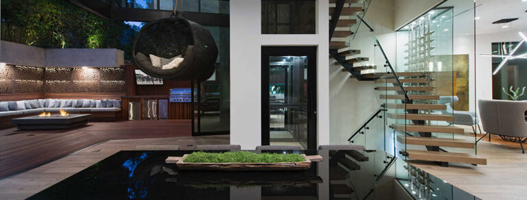 Outdoor seating by a pond beside floating stairs and a dark framed lift door, Sunset Strip