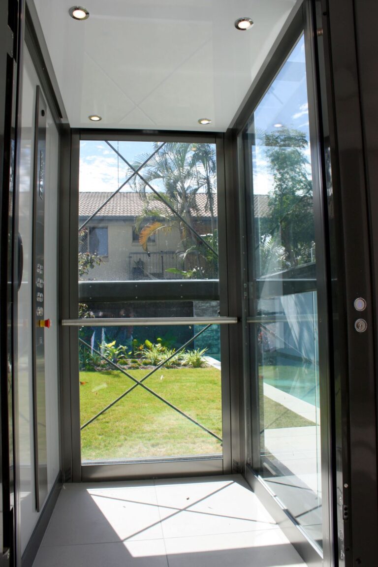 Inside a glass lift car looking out to a lawn through a cross braced glass wall
