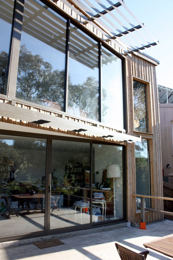 Glass fronted Fairfield home with timber cladding and a louvred sunshade, seen from the garden