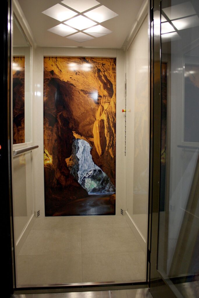 Inside the E1 home lift in Fairfield, with a cave mural on the rear wall and a diamond pattern ceiling light