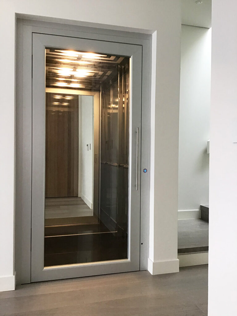 Silver framed glass lift door with a timber panelled cabin and downlights in a hallway