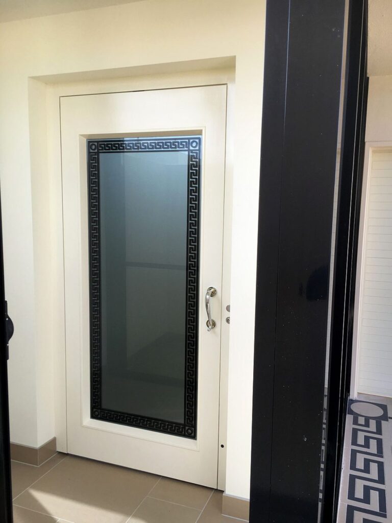 White lift landing door with a Greek key glass panel and chrome handle at Palazzo Versace