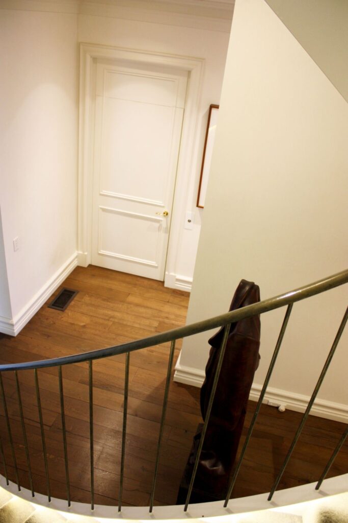 Looking down past a curved balustrade to the white panelled lift door on the timber floor