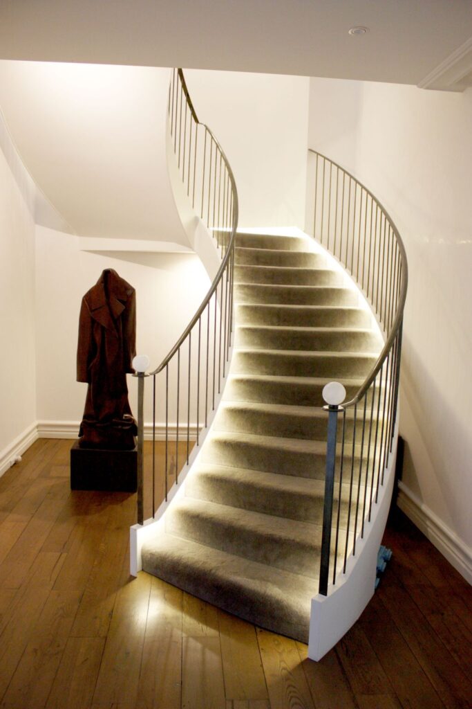 Curved staircase with carpet and lit steps beside a timber floor in the Sydney Harbour home