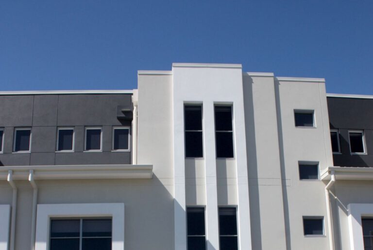 White rendered townhouse facade with tall narrow windows and a grey upper level