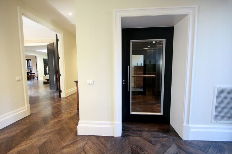 Black framed lift door with a glass panel at the end of a parquet hallway