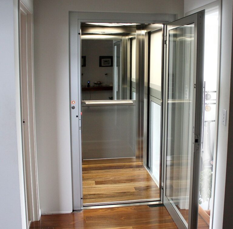Open glass lift door showing the timber floored cabin and the mirror on the back wall