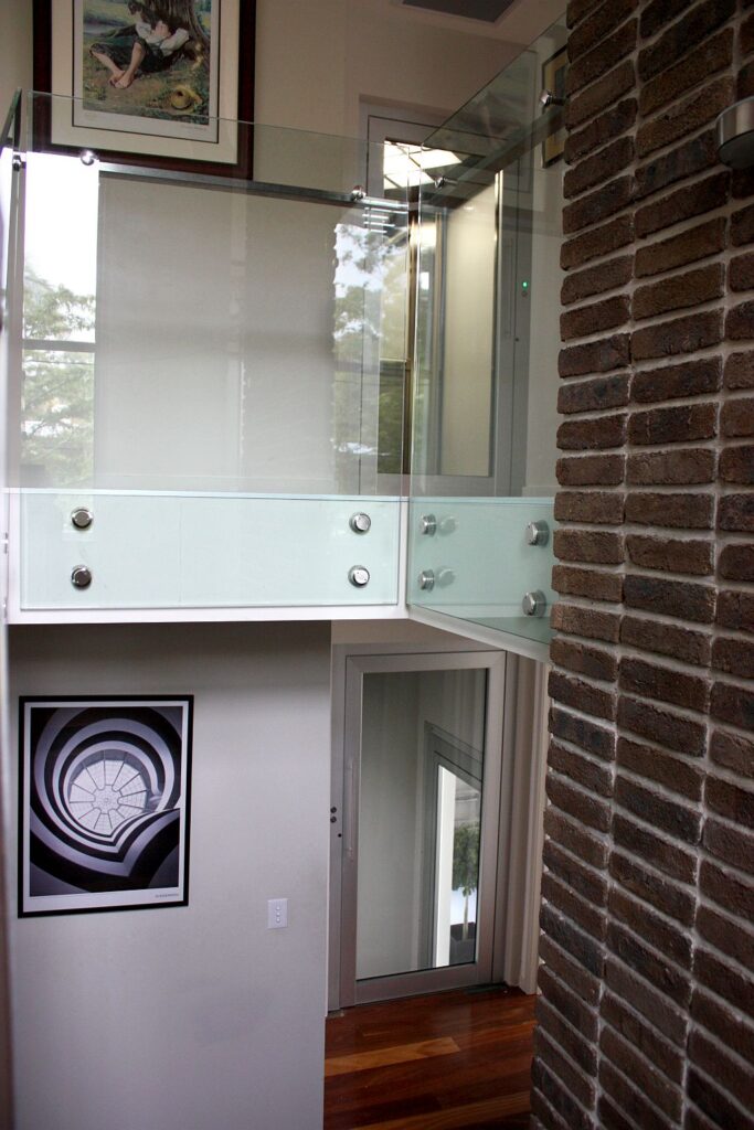 Glass fronted lift beside a dark brick wall with a framed artwork below
