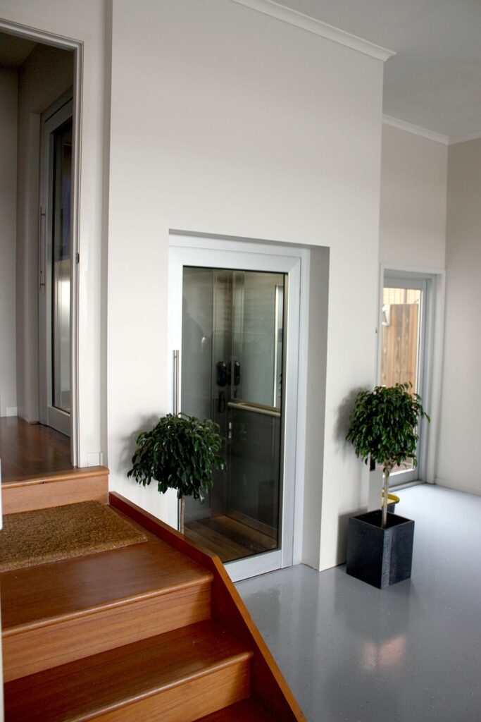 Timber steps leading up to the glass lift door in a hallway with a potted plant
