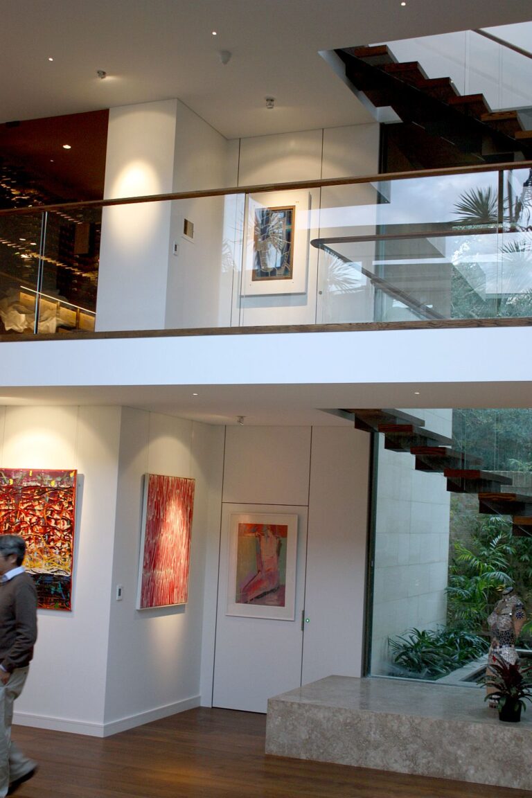 Ground level and first floor landings, each with a flush white lift door set beside framed artwork