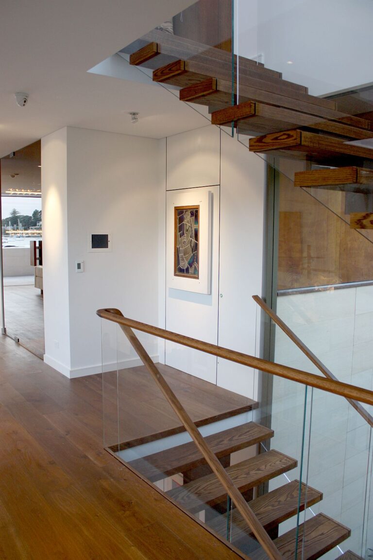 First floor landing with a custom leadlight door that doubles as the lift handle, beside a floating timber staircase