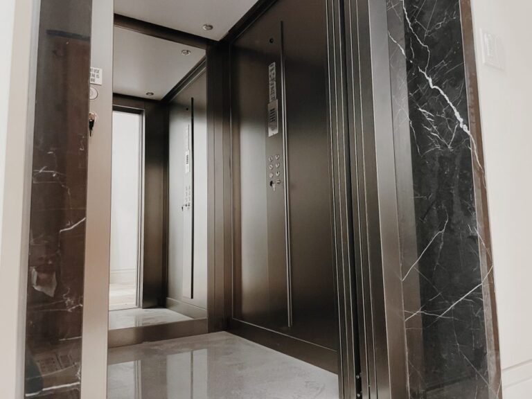 Lift car with dark bronze walls and black marble trim, doors open onto a stone floor