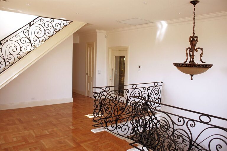 Upper landing with an ornate wrought iron balustrade, a pendant light and a parquet floor in a four-storey Melbourne home
