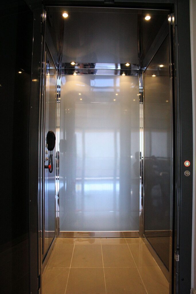 Inside the ElfoLift cabin with a mirrored back wall, polished stainless steel trim, ceiling downlights and a tiled floor