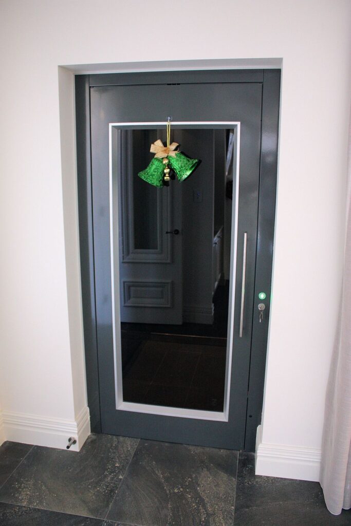 Dark grey ElfoLift landing door with a glass panel and a long handle, in a white doorway in Coogee