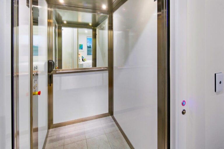 White gloss Elfo E1 cabin seen through the glass door with a half-height mirror, stainless steel frame and tiled floor