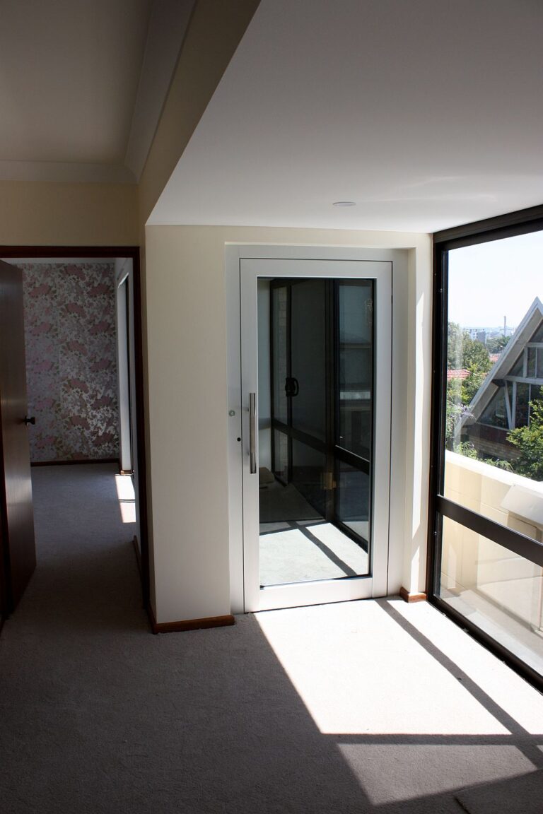 Glass-panelled lift door on an upstairs landing beside a window