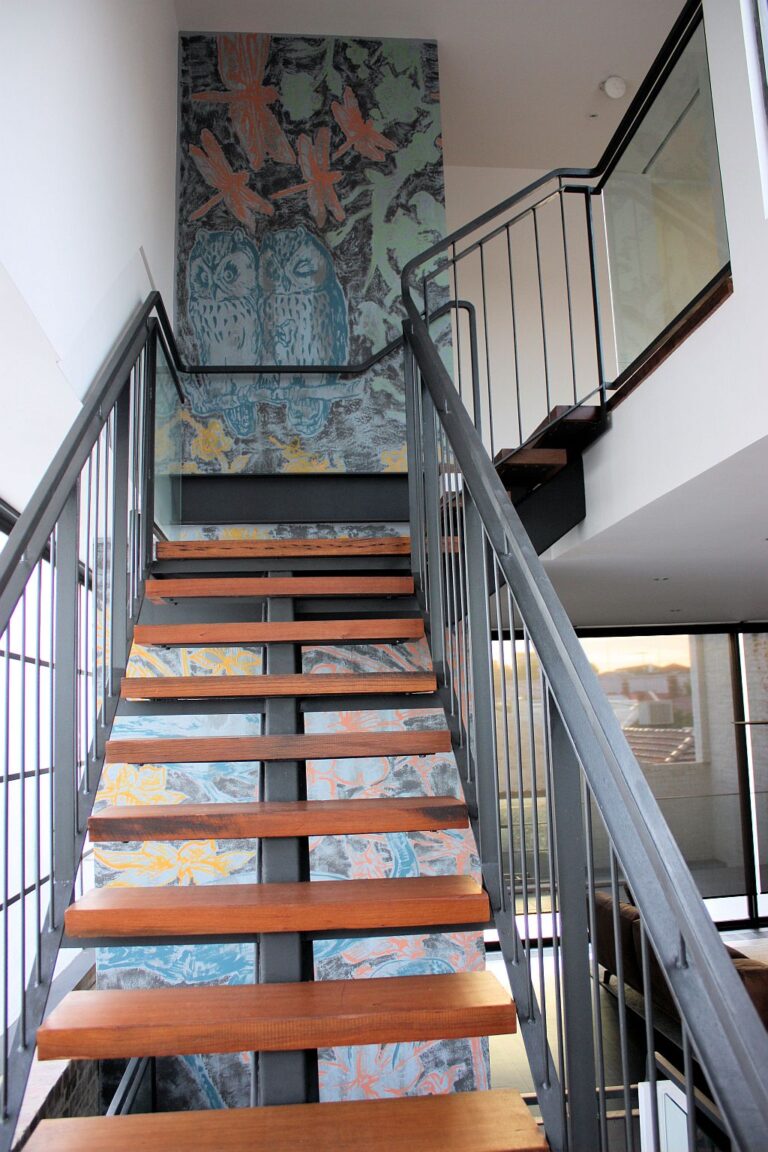 Looking up the stairwell of the Collingwood home past steel stairs and painted artwork on the shaft walls