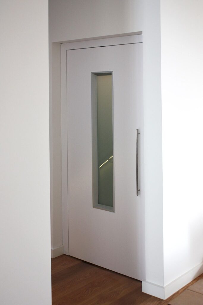 Closed white lift door with a narrow milk glass panel and a stainless pull handle on a timber floor