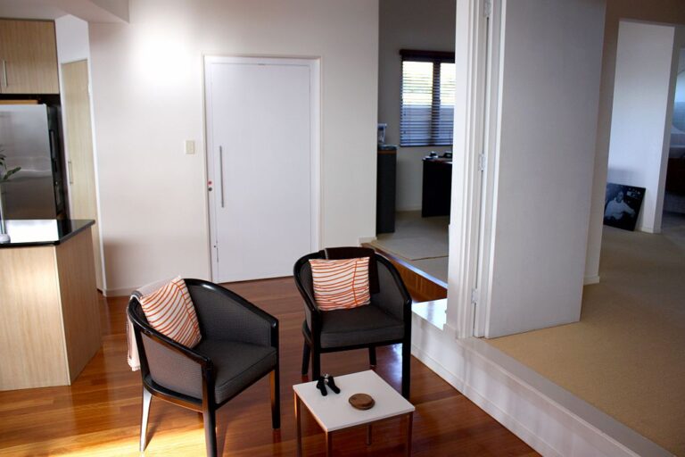 Closed white lift door beside two black armchairs in a living area with timber floor