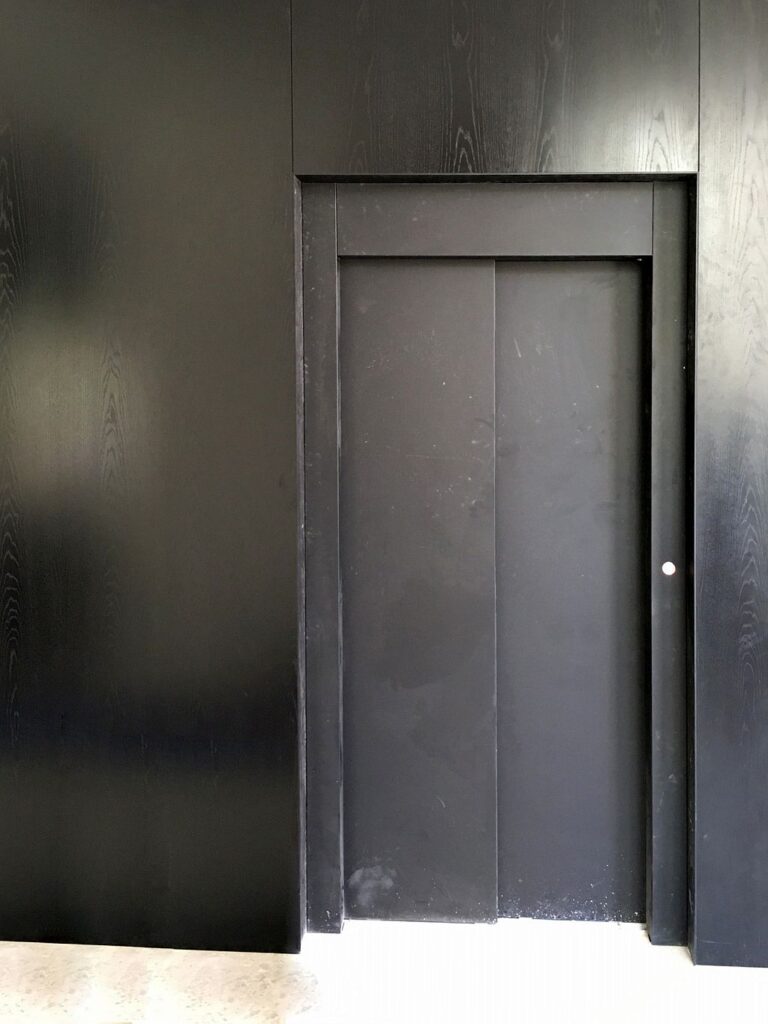 Closed black lift landing door set in black panelling in a Toorak home