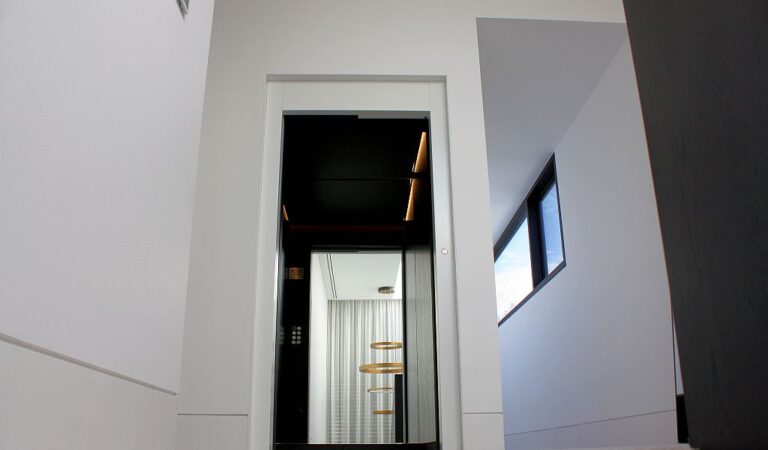 Black lift door seen through a doorway on a white landing in a Toorak home