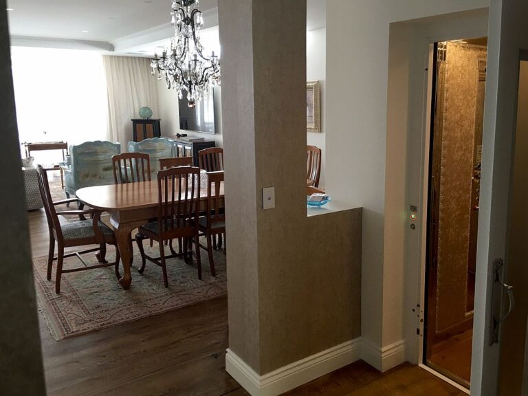 Dining room with a chandelier and the lift door open in the wall beside it