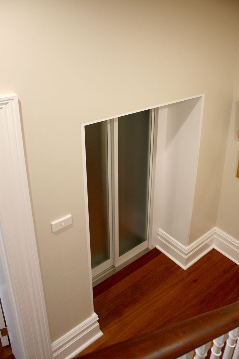 White framed frosted glass lift landing doors set into a hallway wall above a timber floor in the Glebe terrace