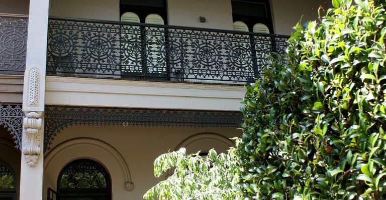 Ornate cast iron balcony balustrade on a terrace home beside a leafy tree in Glebe